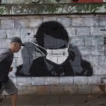 A Man Walks Past A Wall Emblazoned With A Mural Depicting Brazil's President Jair Bolsonaro Putting On A Protective Face Mask With The Portuguese Word For 