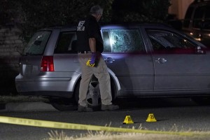 A Washington State Patrol Official Walks Near Evidence Markers And A Car With Broken Windows