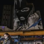 A Woman Wearing A Face Mask To Curb The Coronavirus Walks In Front Of A Mural Created By Street Artist Ino In The Psiri District Of Athens,