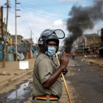 A Police Officer Holds A Pistol During Clashes With Protesters Near A Barricade Of Burning Tires In The Kariobangi Slum Of Nairobi, Kenya,