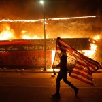 A Protester Carries A U.s. Flag Upside Down As He Walks Past A Burning Building In Minneapolis On May 28, 2020