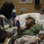 Becky Gonzalez, left, and her long time friend, Mary Lou Samora, a 71-year-old COVID-19 patient, put their palms together after they shared some encouraging words at Providence Holy Cross Medical Center in Los Angeles, Friday, Dec. 17, 2021. (AP Photo/Jae C. Hong)