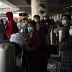 Travelers wait for a shuttle but to arrive at the Los Angeles International Airport in Los Angeles, Monday, Dec. 20, 2021. The Los Angeles County Department of Public Health reported more than 3,500 new cases of COVID-19 on Sunday as the number of daily new cases tripled over the week. (AP Photo/Jae C. Hong)