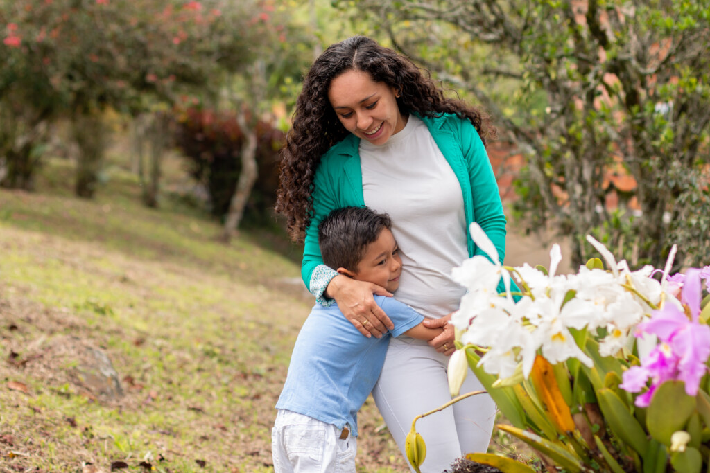 Mother And Son Happily Embracing In A Natural Park Next To Beautiful Orchids