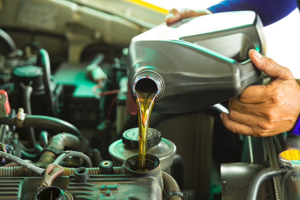 Car,mechanic,replacing,and,pouring,fresh,oil,into,engine,at