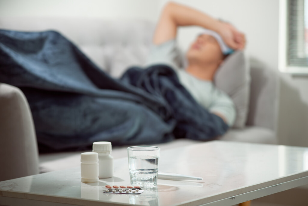 Sick Wasted Man Lying In Sofa Suffering Cold And Winter Flu Virus Having Medicine Tablets In Health Care Concept Looking Temperature On Thermometer