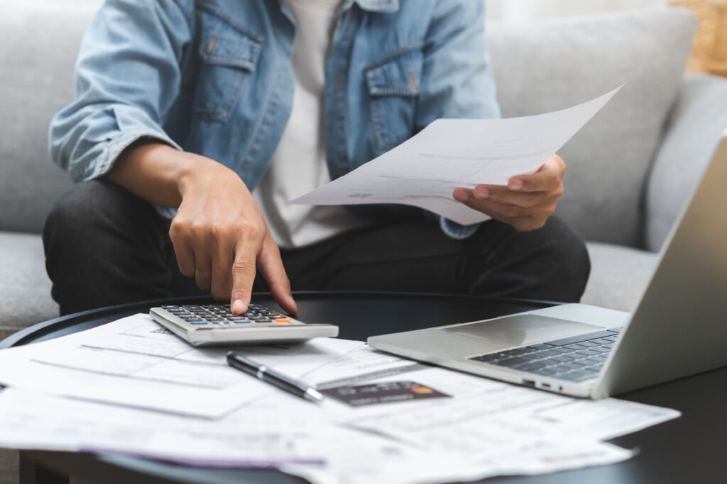 Business Financial Concept, Owe Asian Young Man, Male Sitting On Couch Stressed Hand Calculate Expense On Table At Home From Invoice Or Bill Have No Money To Pay Mortgage Or Loan, Debt Bankruptcy.