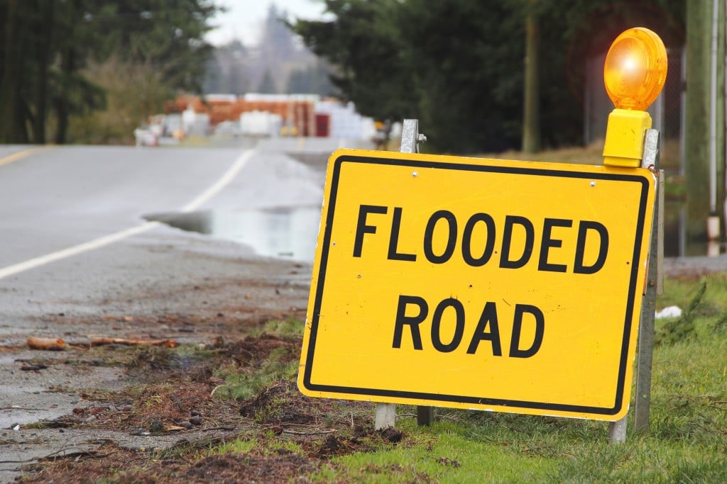 A bright yellow sign warns motorists that the road is flooded.