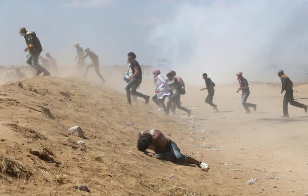 A Palestinian demonstrator reacts as others run from tear gas fired by Israeli forces during a protest marking the 70th anniversary of Nakba