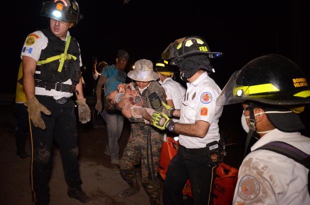 A volunteer firefighter carries a child after the eruption of the Fuego Volcano