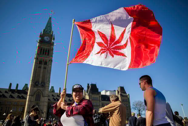 A woman waves a flag with a marijuana leef on it next to a group gathered to celebrate National Marijuana Day on Parliament Hill in Ottawa