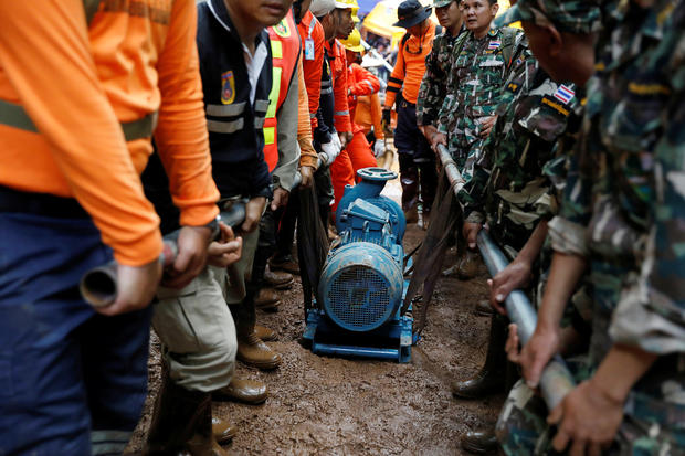 Soldiers and rescue workers carry a water pump to the Tham Luang cave complex during a search for members of an under-16 soccer team and their coach
