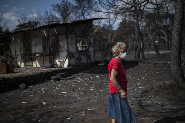 TOPSHOT - A woman wearing a mask walks in front of her burnt house following a wildfire at the village of Neos Voutzas