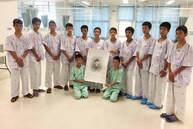 The 12-member "Wild Boars" soccer team and their coach rescued from a flooded cave pose with a drawing picture of Samarn Kunan