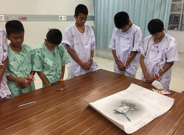 Members of "Wild Boars" soccer team and their coach rescued from a flooded cave bow their heads after writing messages on a drawing picture of Samarn Kunan at the Chiang Rai Prachanukroh Hospital 