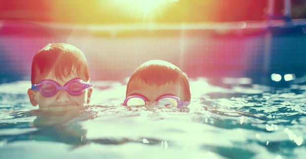 Two little kids in goggles swimming in pool at vintage sunset