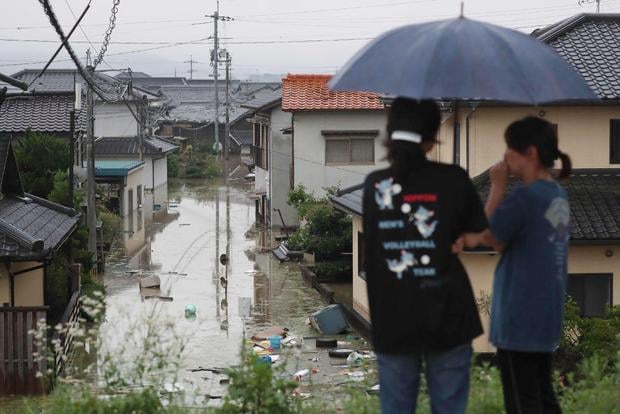 Residents look at a flooded road and houses in Kurashiki