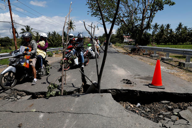 A family rides on a motorcycle through a crack on the street at Kayangan district after earthquake hit on Sunday in North Lombok