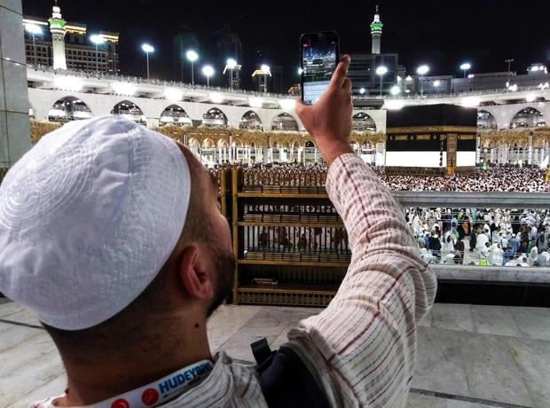 A Muslim worshipper uses his cell phone to livestream film others circumambulating around the Kaaba