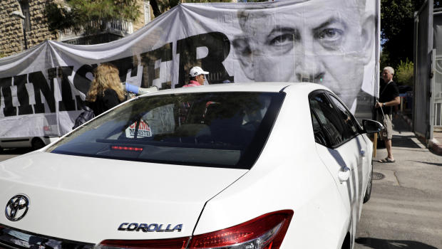 Israeli protesters hold signs as police interrogators arrive to the Prime Minister's residence in Jerusalem