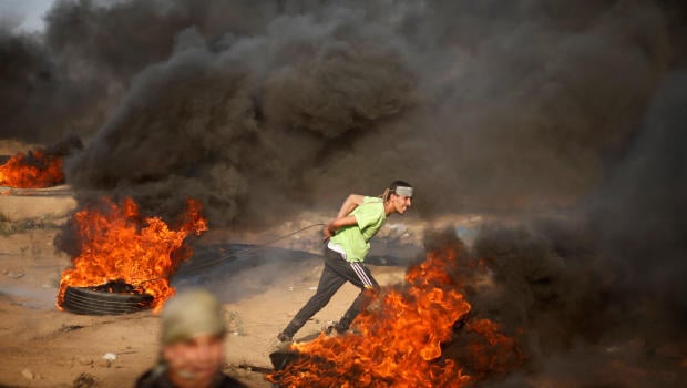 A Palestinian demonstrator pulls a burning tyre during a protest calling for lifting the Israeli blockade on Gaza and demanding the right to return to their homeland