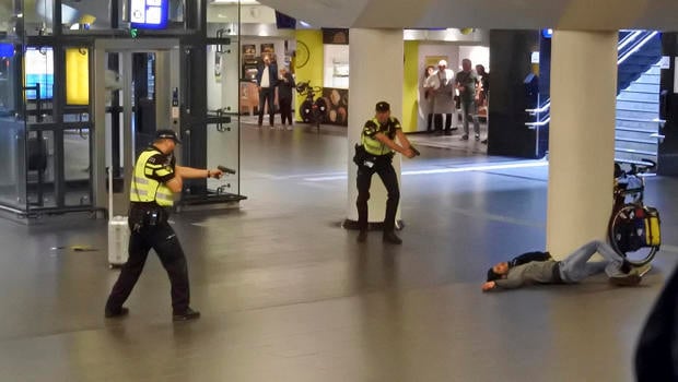 Dutch police officers point their guns at a wounded 19-year-old man who was shot by police after stabbing two people in the central railway station in Amsterdam