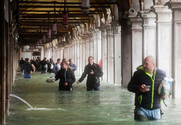 Tourists under arches next to the flooded St Mark's Square during a high-water (Acqua Alta) alert in Venice on October 29