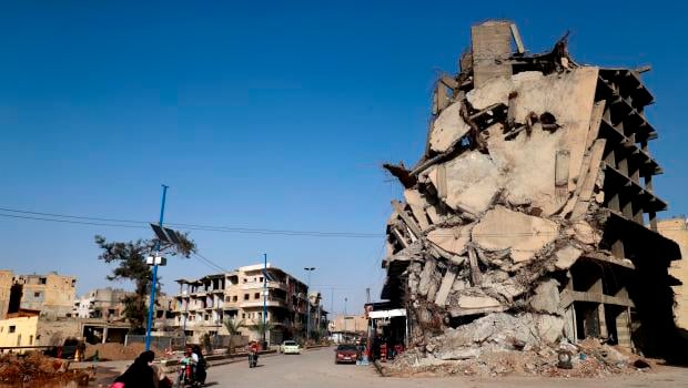TOPSHOT - Syrians ride their motorcycles past a damaged building in the Syrian city of Raqa on October 18