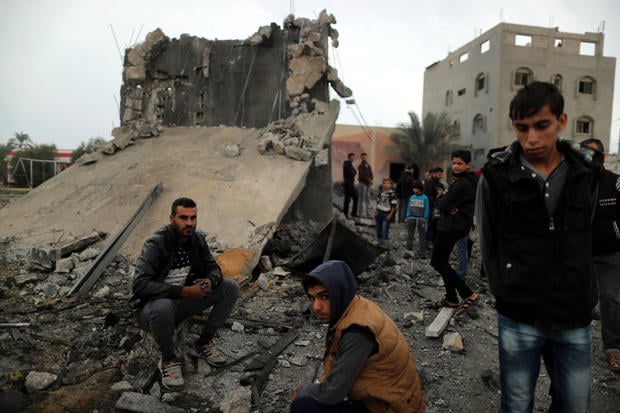 Palestinians sit at the remains of a building that was destroyed by an Israeli air strike
