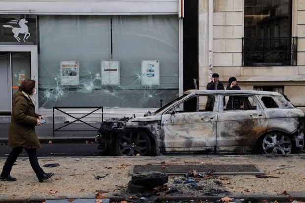 People stand next to a charred car in a street of Paris on December 2