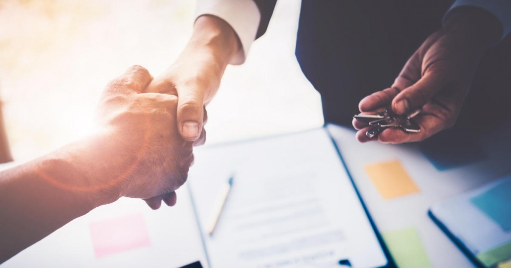 Agents are giving house keys of customer with handshaking after good deal at agency office. Real Estate and Agreement concept.