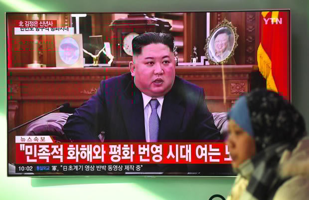 A woman walks past a television news screen showing a New Year speech by North Korean leader Kim Jong Un at a railway station in Seoul on January 1