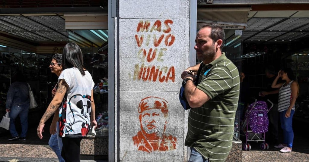 People walk past a stencil depicting late Venezuelan President Hugo Chavez and a legend reading "More alive than ever" in Caracas on February 01