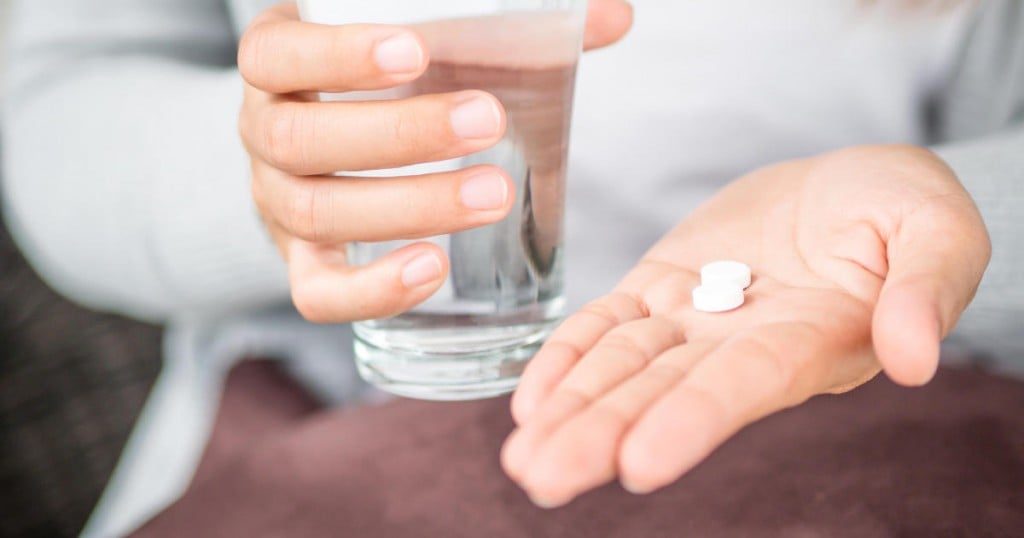 Closeup woman hand with pills medicine tablets and glass of water for headache treatment. Healthcare