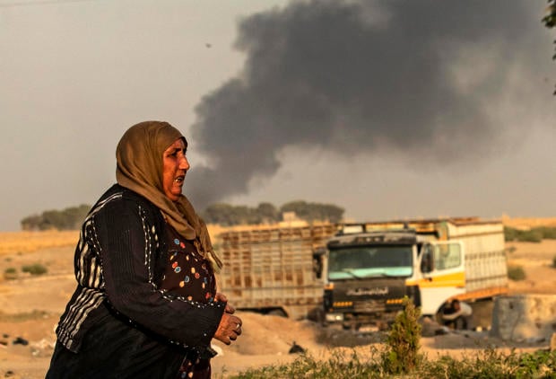 TOPSHOT - A woman walks as smoke billows following Turkish bombardment in Syria's northeastern town of Ras al-Ain in the Hasakeh province along the Turkish border on October 9
