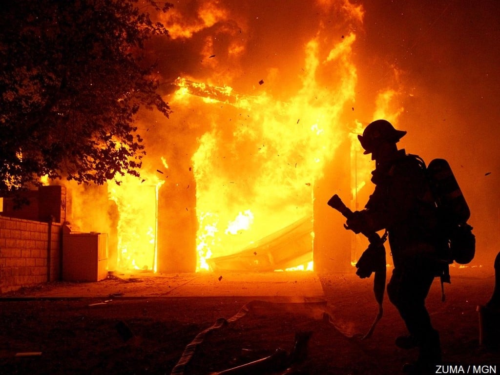 A firefighter prepares to put water on a fully engulfed house fire in Canyon Country