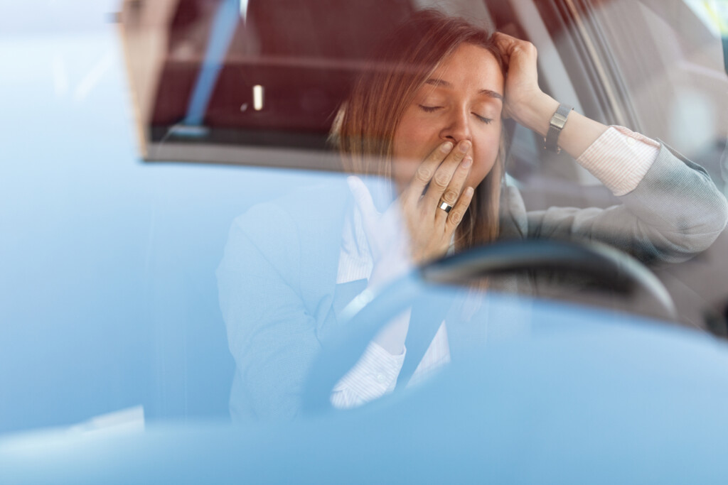 Young Businesswoman Yawning Behind The Steering Wheel.