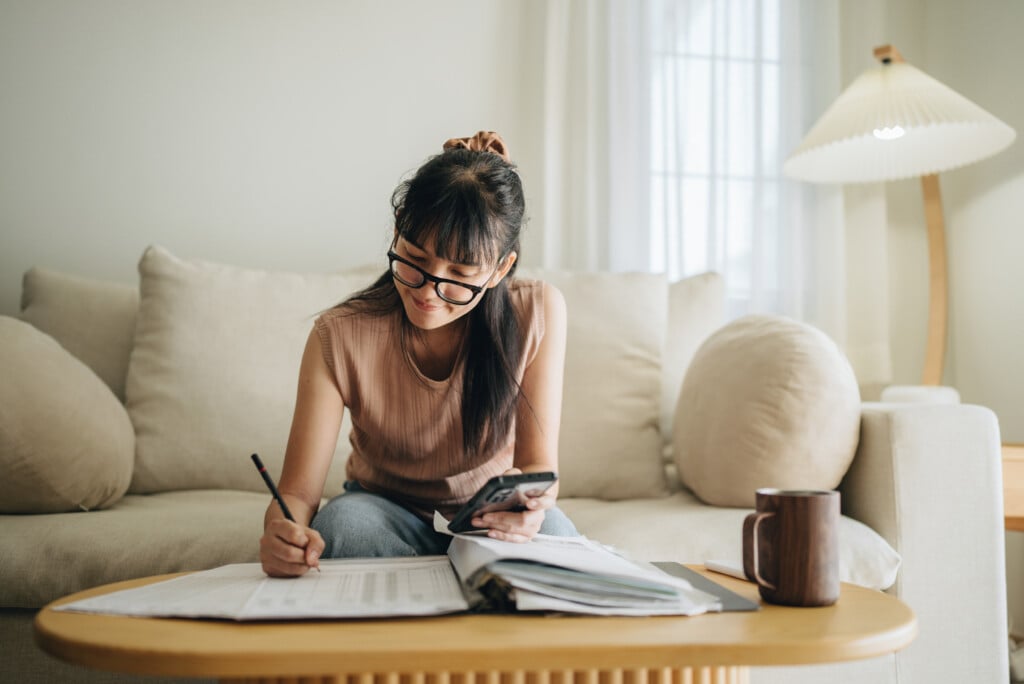 Asian Woman Planning Budget And Using Calculator On Smartphone.