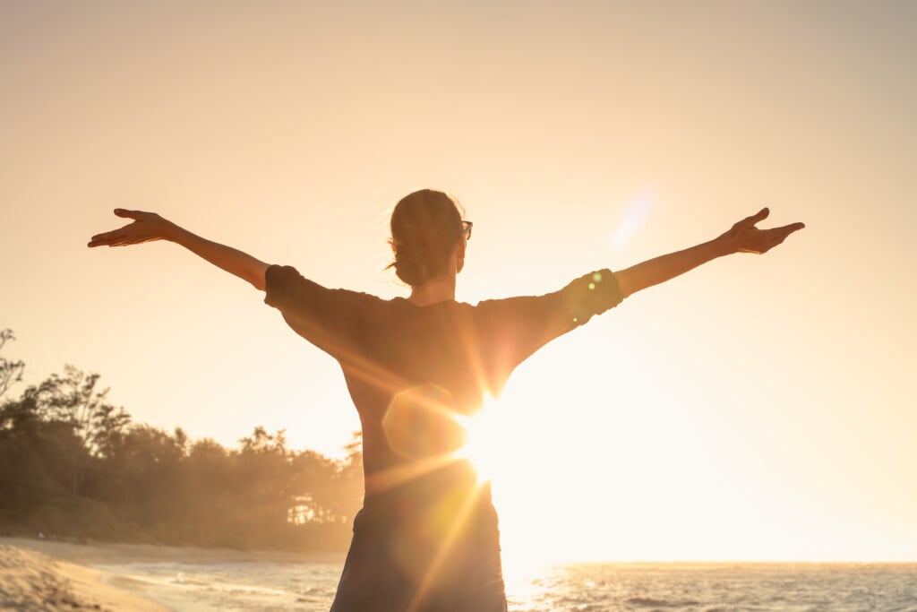 Young Woman Basks In Sunsets Warm Rays Of Sunshine With Outstretched Arms.