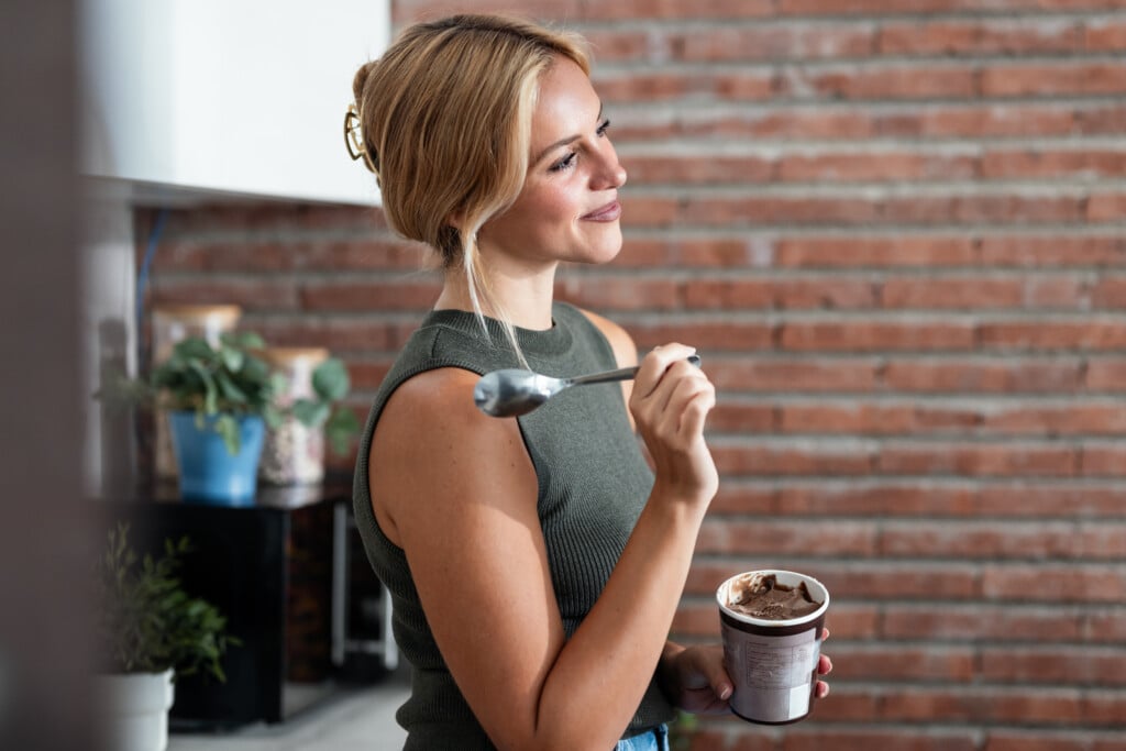 Beautiful Young Woman Eating Chocolate Ice Cream In The Kitchen At Home