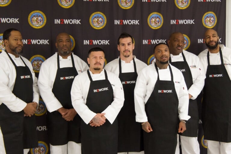 Inmates at Eastern Correctional Institution stand in front of the IN2WORK and Maryland Department of Public Safety and Correctional Services backdrop.