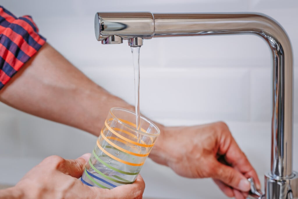 Man Pouring Glass Of Water From Tap With Clean Filter In Kitchen