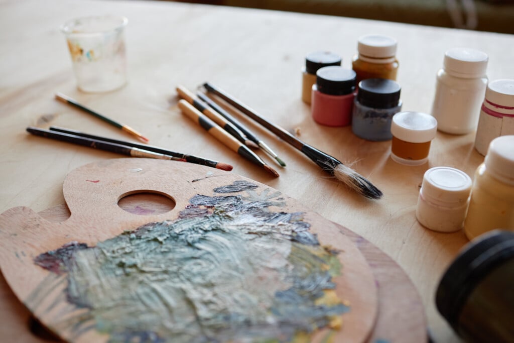 Close Up Of Art Supplies And Paintbrushes Arranged On Wooden Tabletop