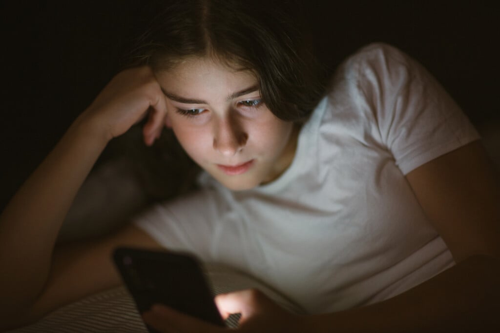 Child Teenager Girl Lies In Bed In Evening Or At Night And Looks Into Phone. Mobile Addiction.