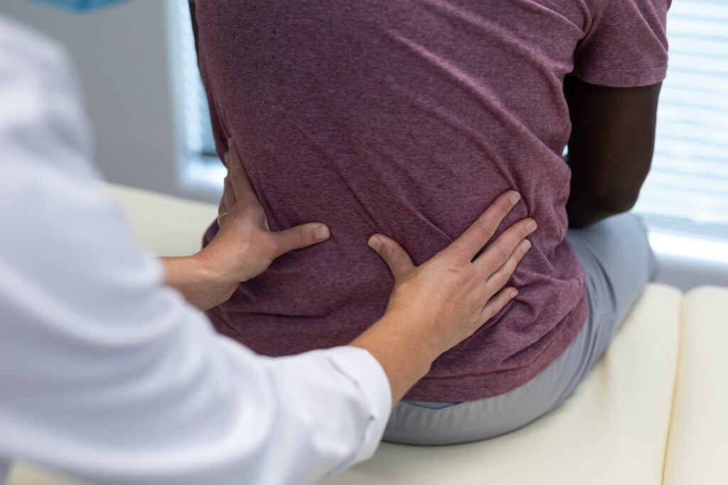 Midsection Of Caucasian Female Physiotherapist Palpating Back Of African American Male Patient. Medicine, Health And Healthcare Services