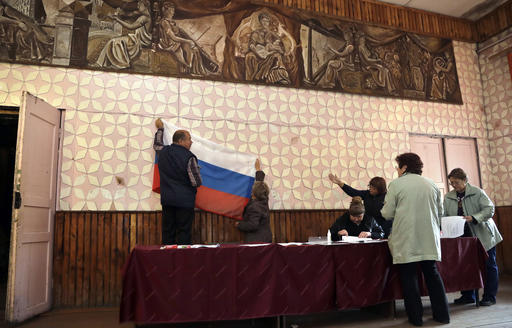 Election officials place a Russian state flag at a polling station ahead of Sunday's parliamentary elections in the village of Gusino