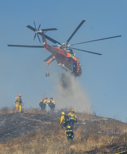 Firefighters battle a brush fire on the ground and from the air on a wind driven fire that threatened homes in the area Wednesday