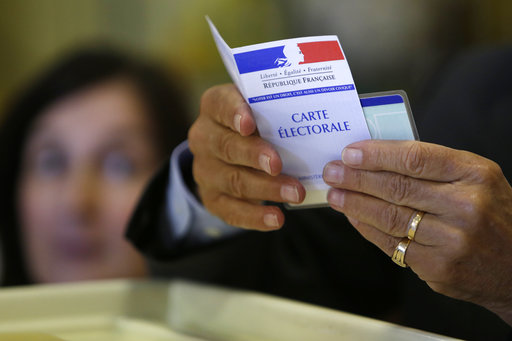 An official holds a voter registration card as people queue to cast their ballots in the presidential runoff election between Emmanuel Macron and Marine Le Pen