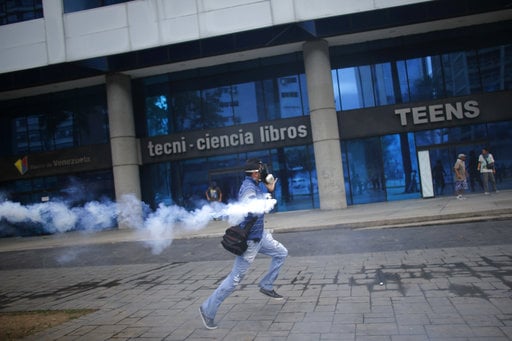 An anti-government protester runs with a canister of tear gas fired by police in Caracas