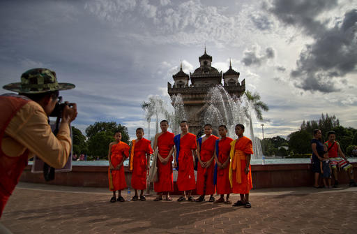 Buddhist monks pose for pictures standing in front of Patuxary Victory Gate in Vientiane
